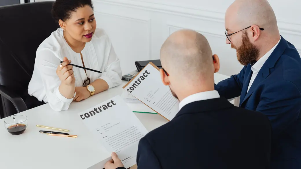 Three professionals reviewing a contract together at a desk during a vendor evaluation meeting