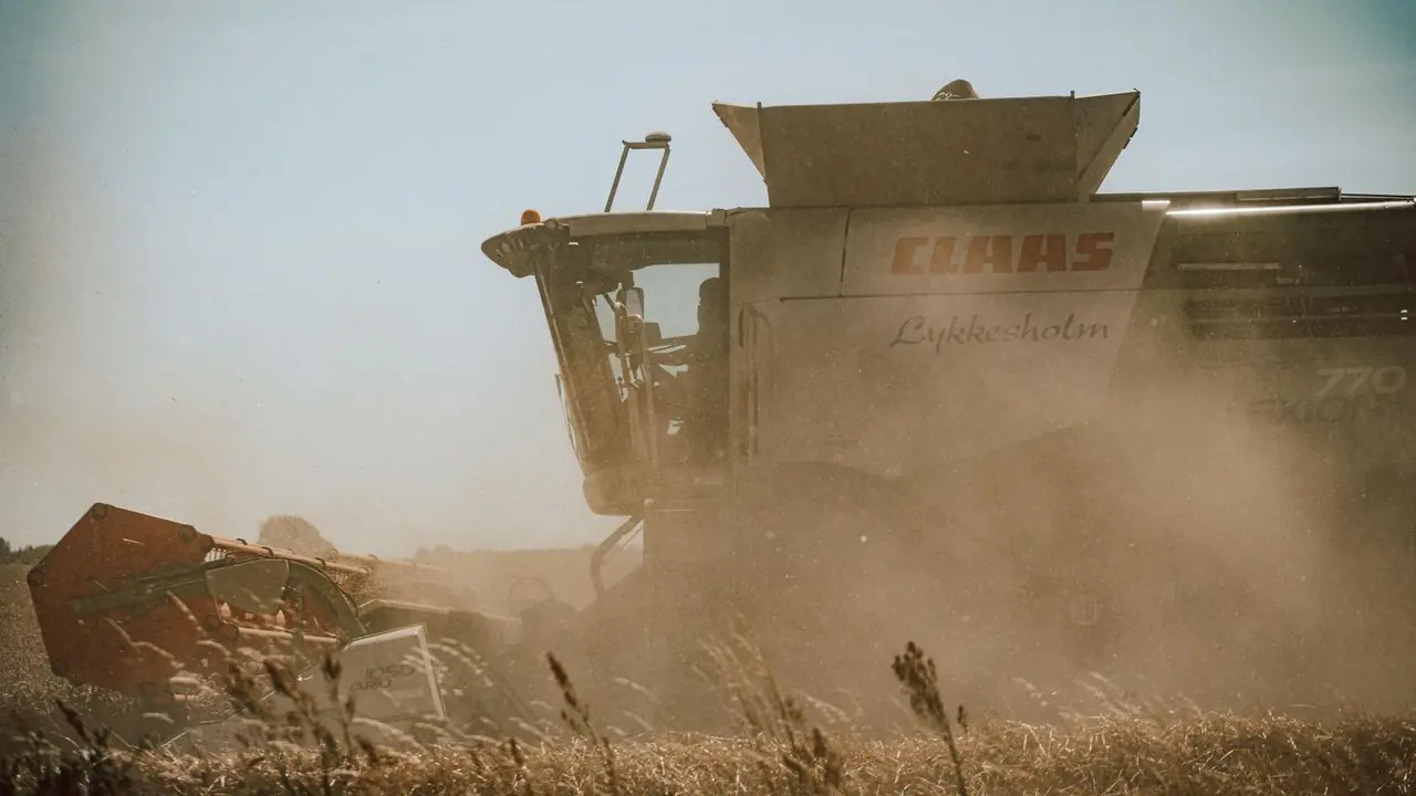 Side view of a combine harvester working in a dusty wheat field during harvest season.