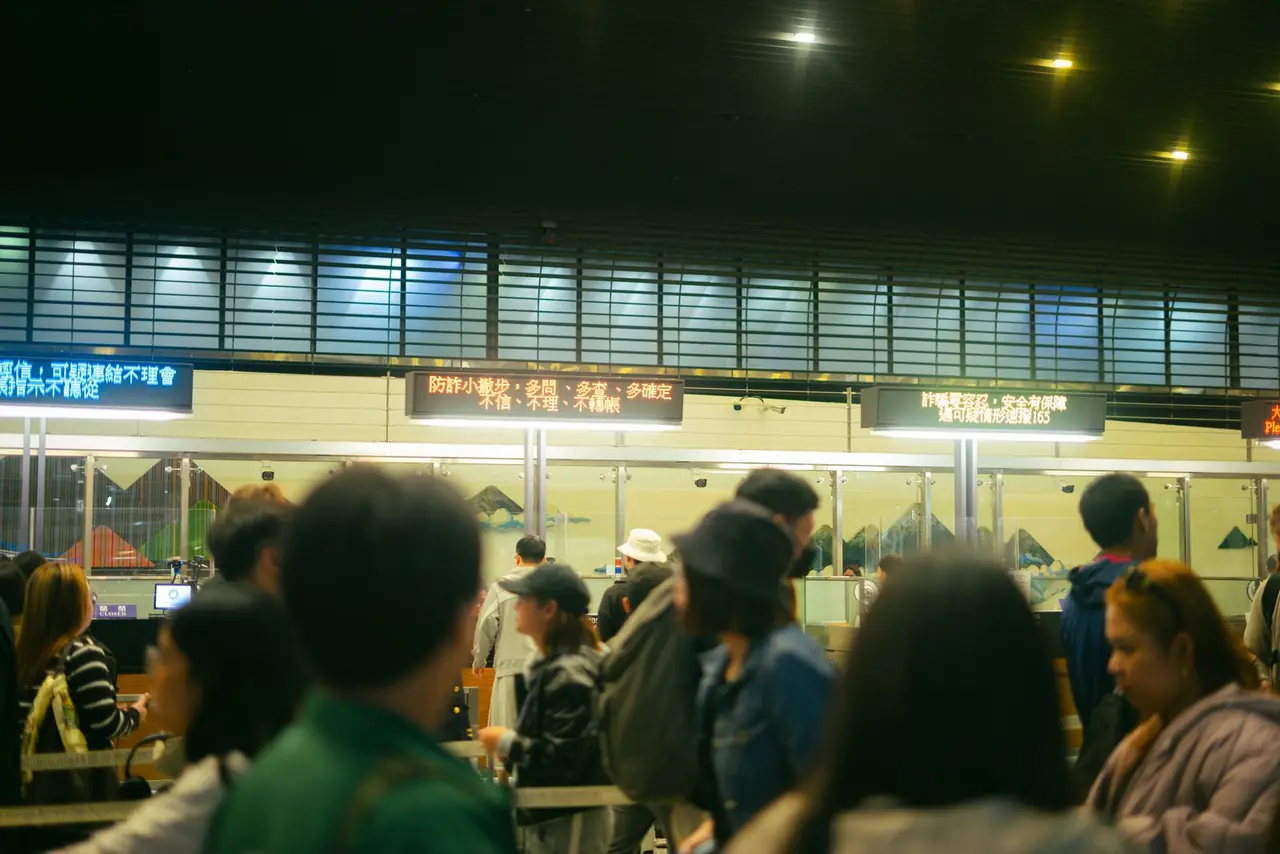 Crowded airport check-in area with people queueing and visible flight information signs.