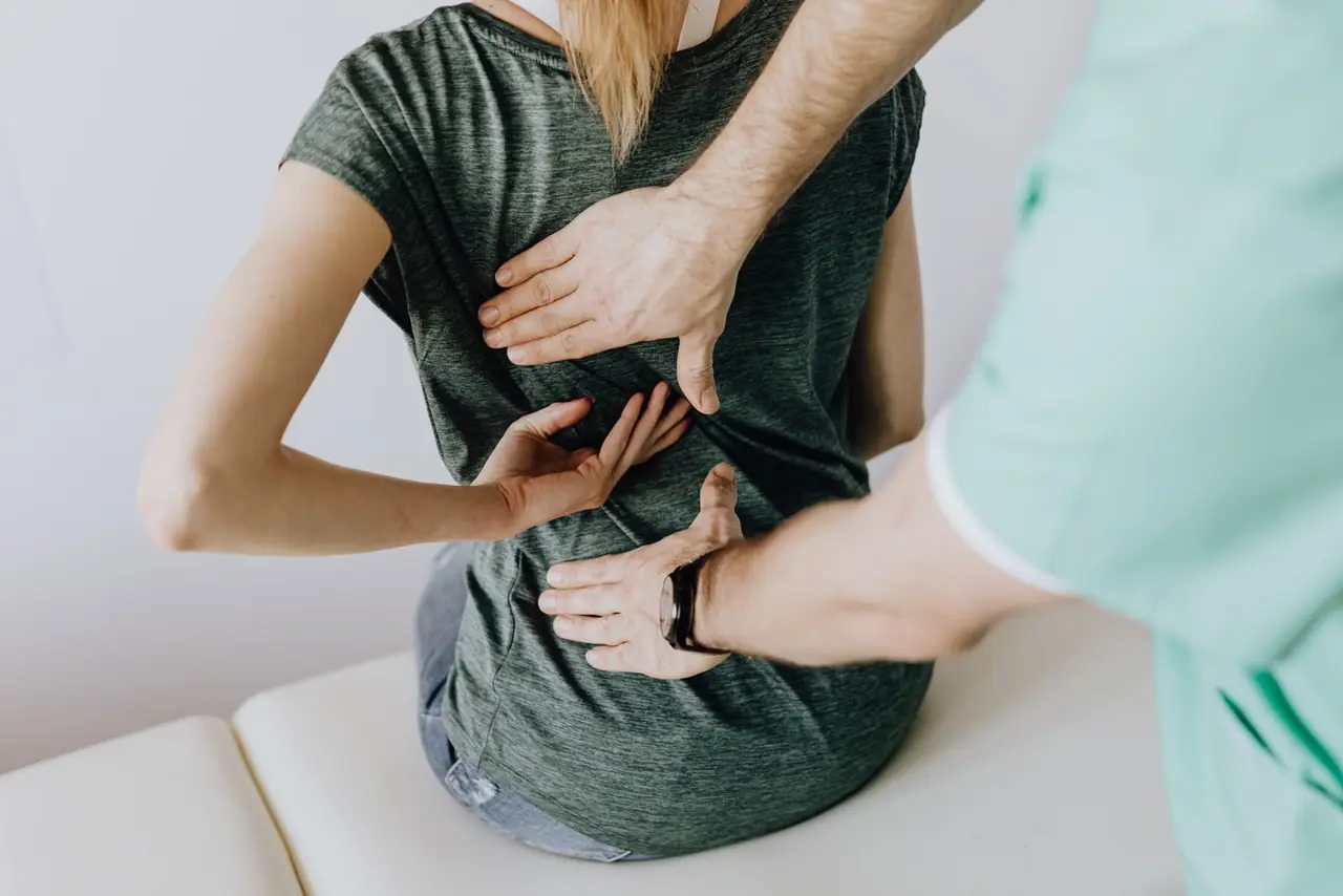 From above of crop faceless slim female patient sitting on examination couch and indicating osteopath in unifo