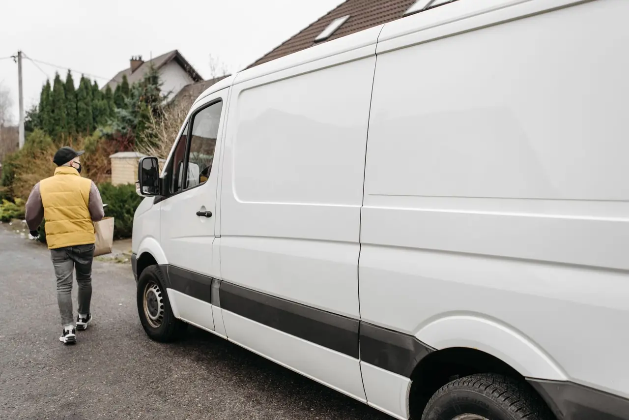 A delivery person carrying a package away from a delivery van outdoors, showcasing efficient logistics.