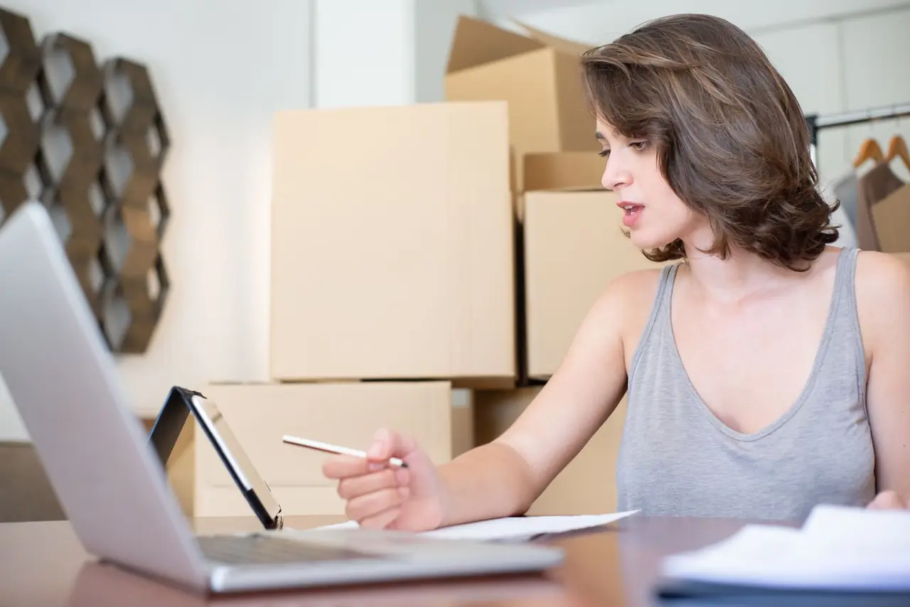 An online store owner working through orders on a laptop, shipping boxes stacked behind her