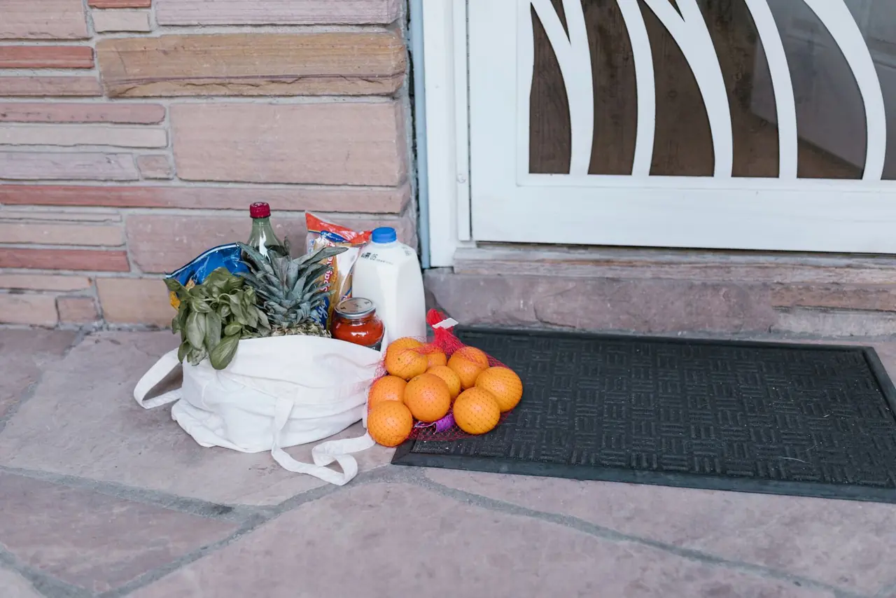 Reusable bag with groceries and fruits left at doorstep, highlighting delivery service.