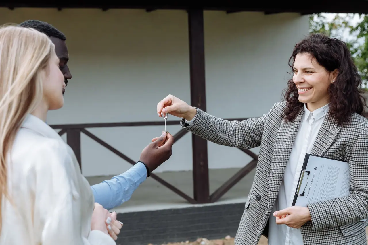 A real estate agent handing house keys to a couple outside a home