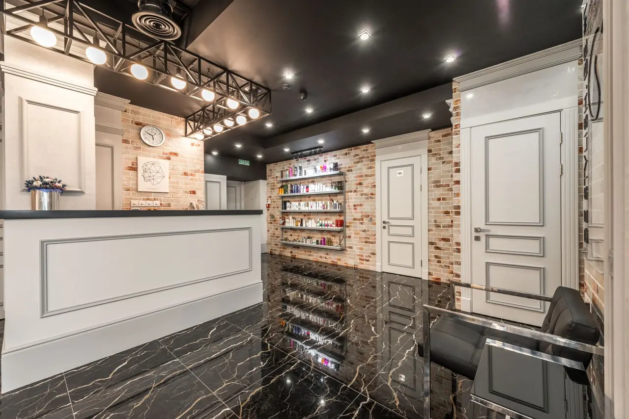White reception counter with flowers placed in stylish beauty salon with doors and shelves with various cosmet