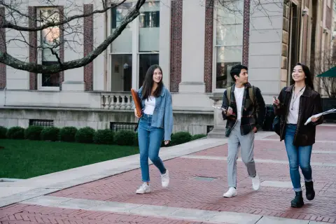 Group of young students walking on campus sidewalk on a bright day, showcasing casual university life.