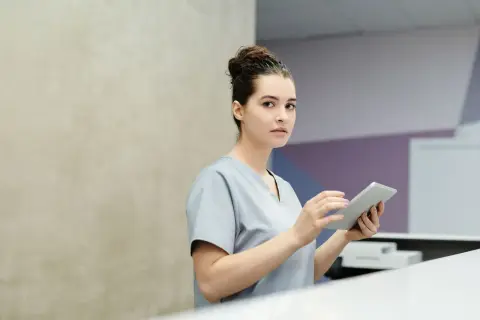 Professional receptionist using a tablet device at a modern office reception desk.