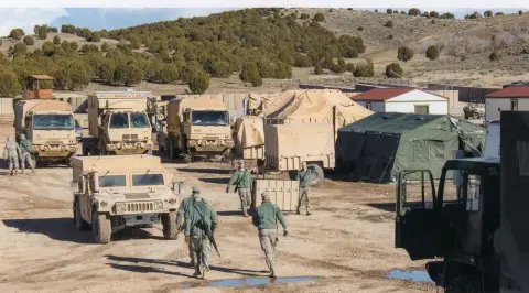 Military vehicles and tents at a training camp in Afghanistan under clear skies.
