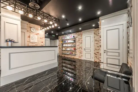 White reception counter with flowers placed in stylish beauty salon with doors and shelves with various cosmet